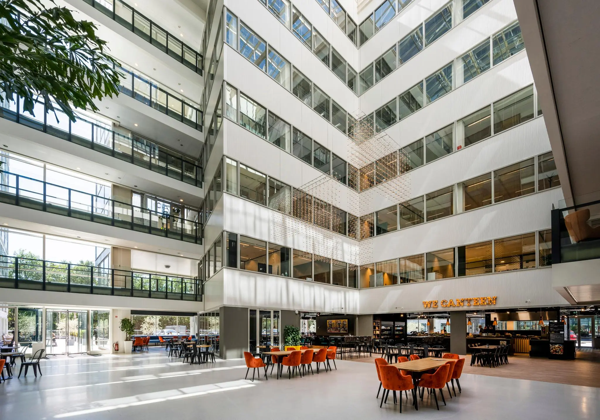 Modern atrium van een kantoorgebouw aan de Thomas R. Malthusstraat met veel glas, natuurlijk licht en een centrale lunchruimte genaamd "We Canteen".